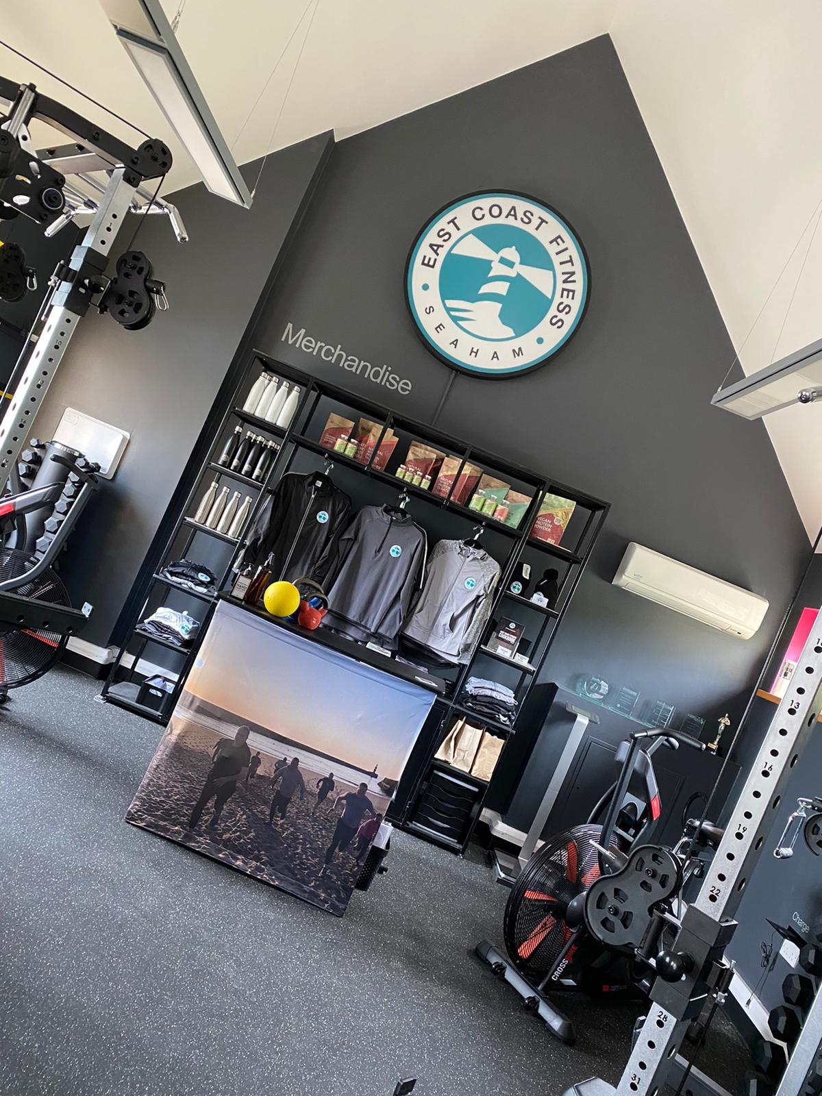 Interior of East Coast Fitness gym showcasing merchandise and fitness equipment, with a large logo on the wall.