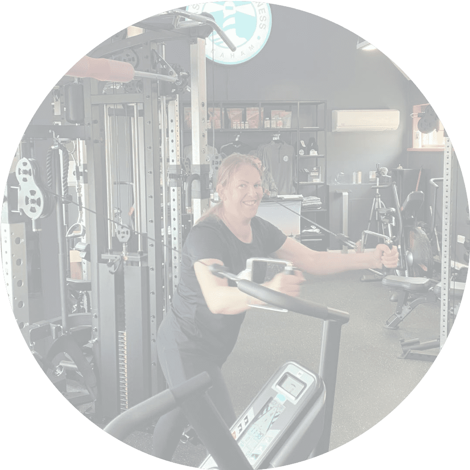 A woman working out in a gym, using a cable machine with a smile, showcasing enthusiasm and fitness.